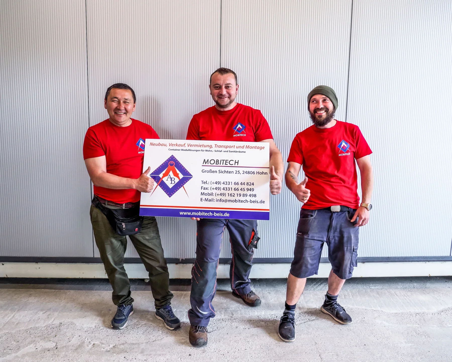 Three people in MOBITECH shirts present a company sign