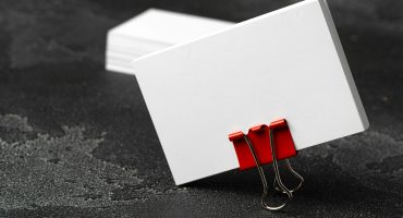 White businesscards united with a paper clip on a black rough background